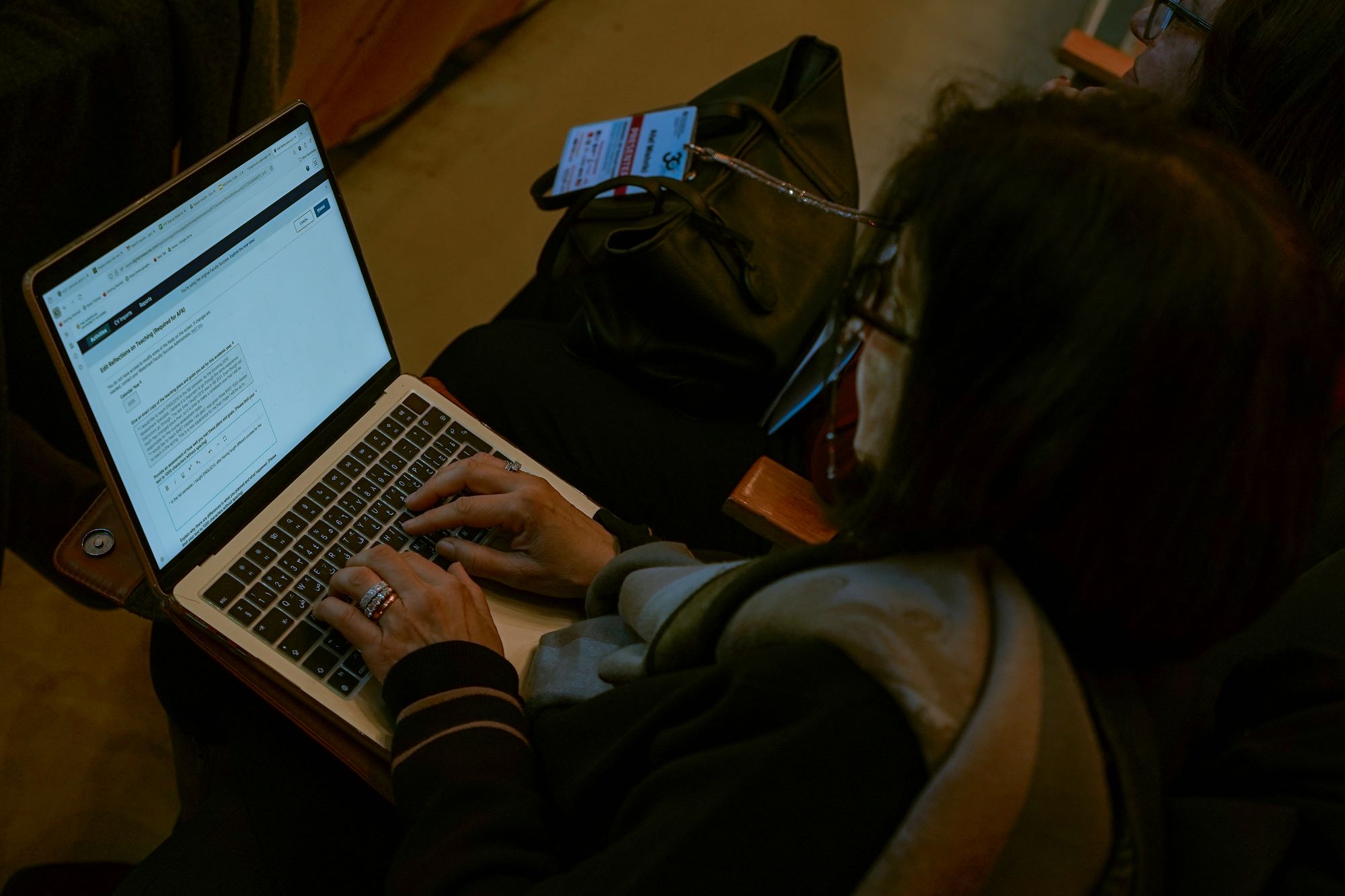 An over-the-shoulder view of a person typing on a laptop computer while sitting in an audience.