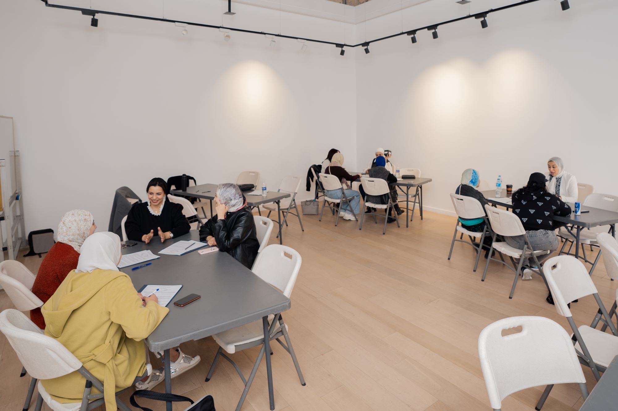 Groups of participants sitting around tables in a bright, modern room, discussing and collaborating during a workshop.