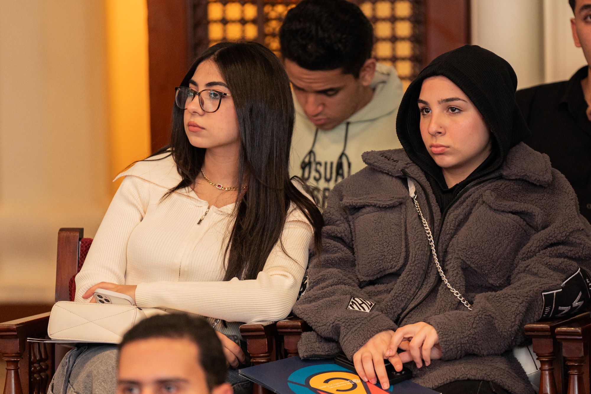 Two young women sitting in an audience and listening attentively during a presentation.