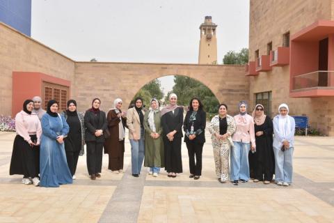 A large group of people posing together for a group photo in an outdoor tiled courtyard with palm trees and pillars.