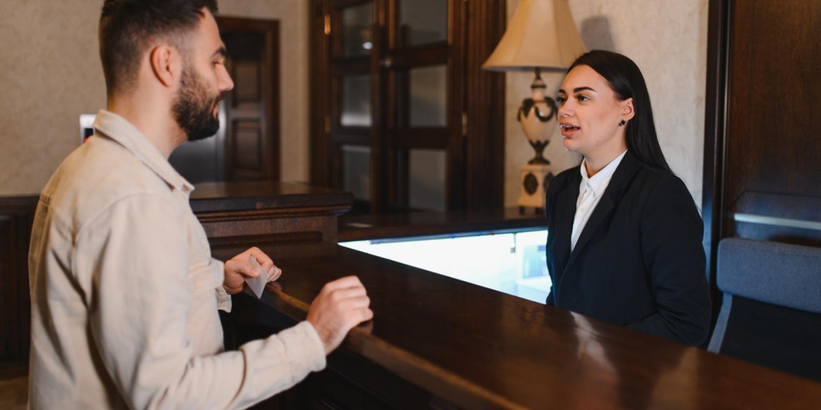 Guest standing at the hotel reception desk, talking to a female receptionist during a vacation or business trip