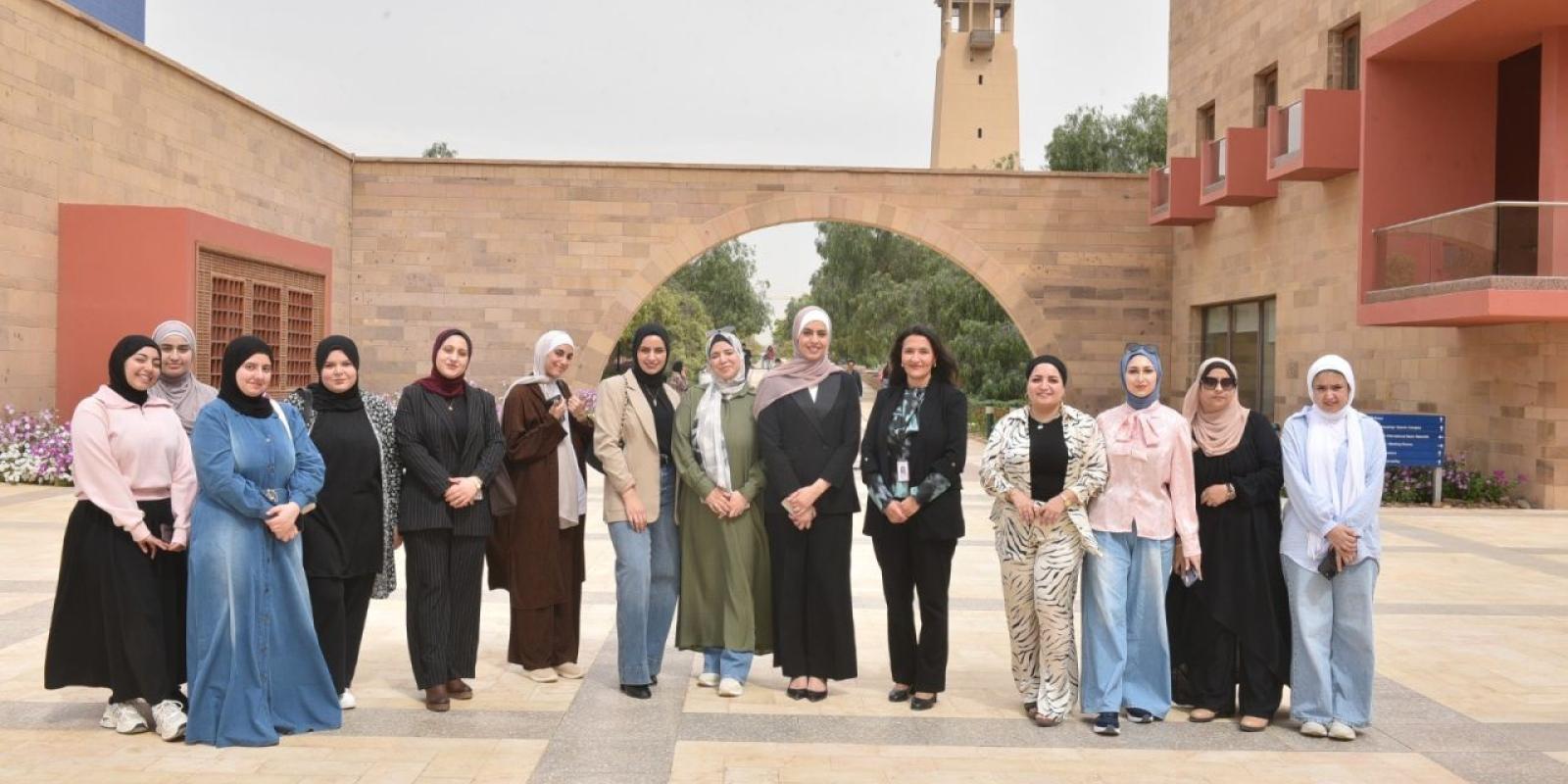 A large group of people posing together for a group photo in an outdoor tiled courtyard with palm trees and pillars.