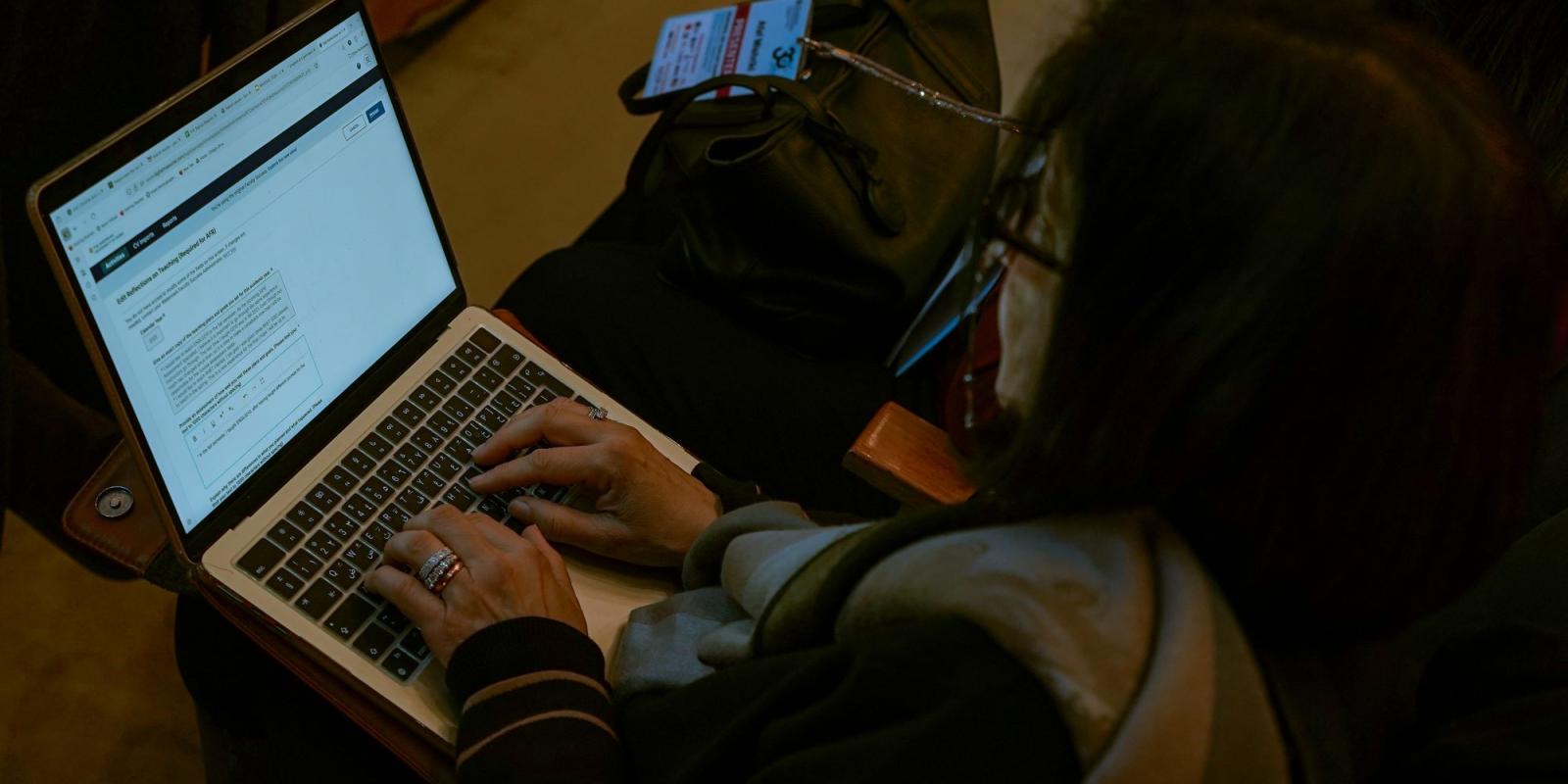 An over-the-shoulder view of a person typing on a laptop computer while sitting in an audience.