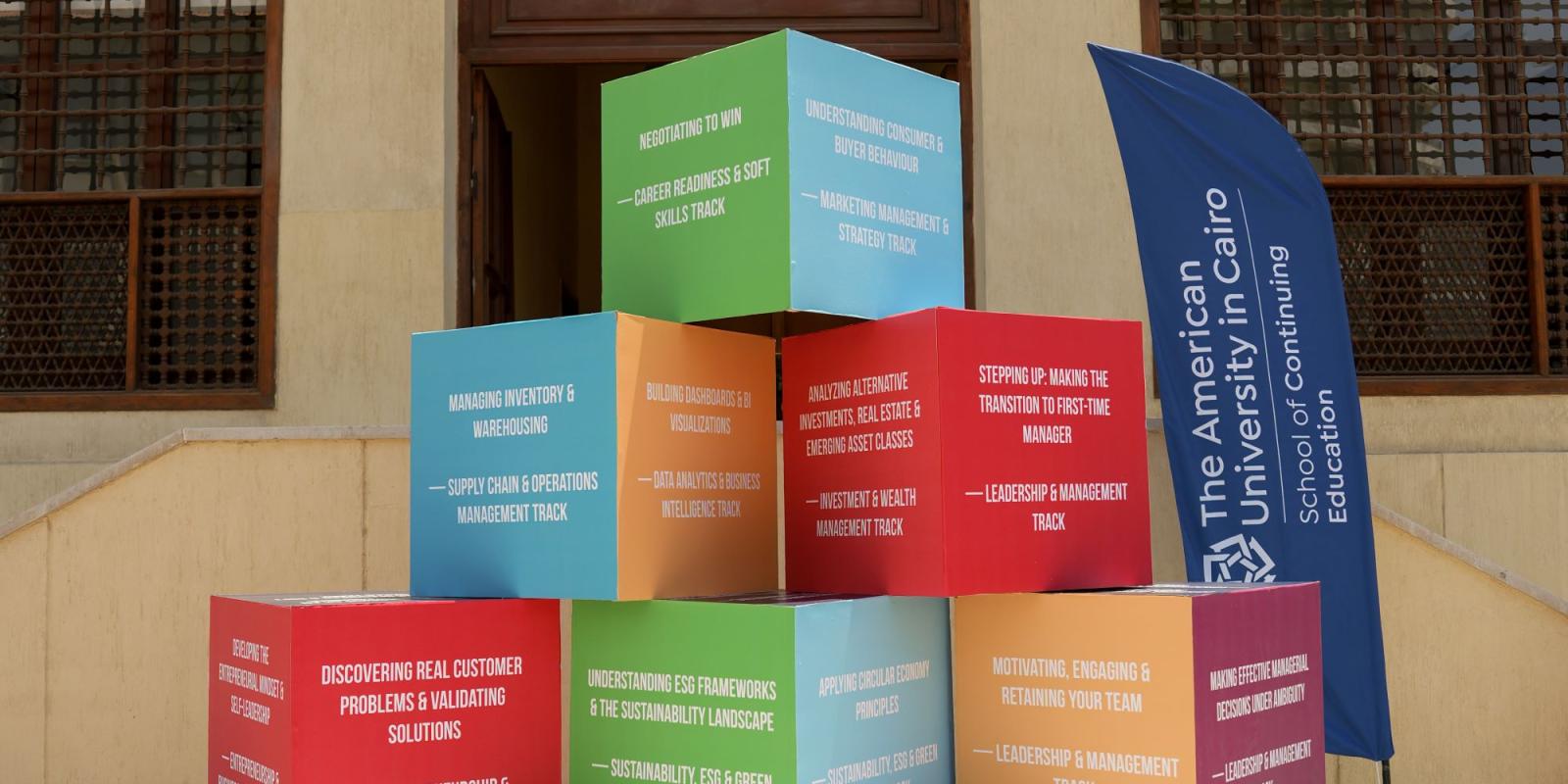 A pyramid of colorful cubes displaying various business and professional development tracks is arranged outdoors on the steps in front of the Oriental Hall building.