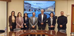 A professional group of men and women pose together in front of a digital screen displaying a photo of The American University in Cairo campus.