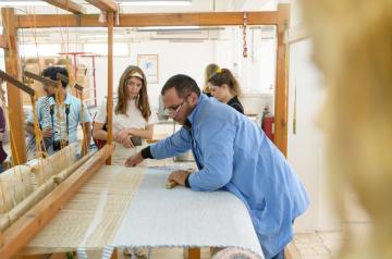 a man weaving a carpet with students